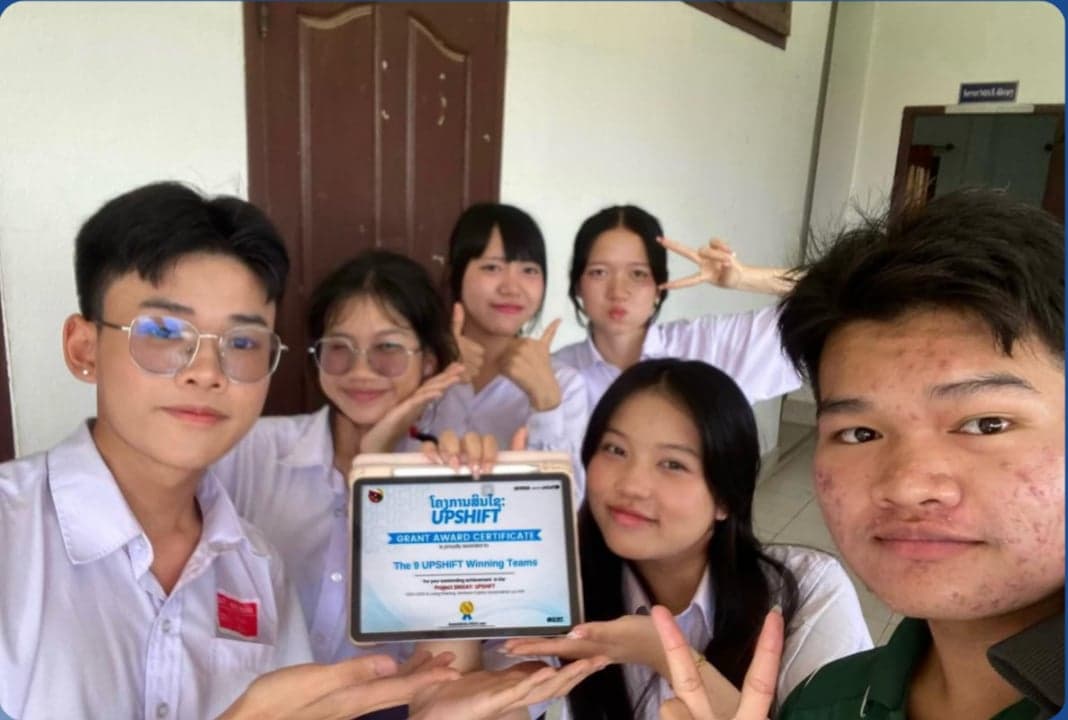 Team Unity Builder, the ODOR.X project from Savannakhet — six participants in a close indoor group selfie, one holding a tablet displaying the winning-teams certificate.
