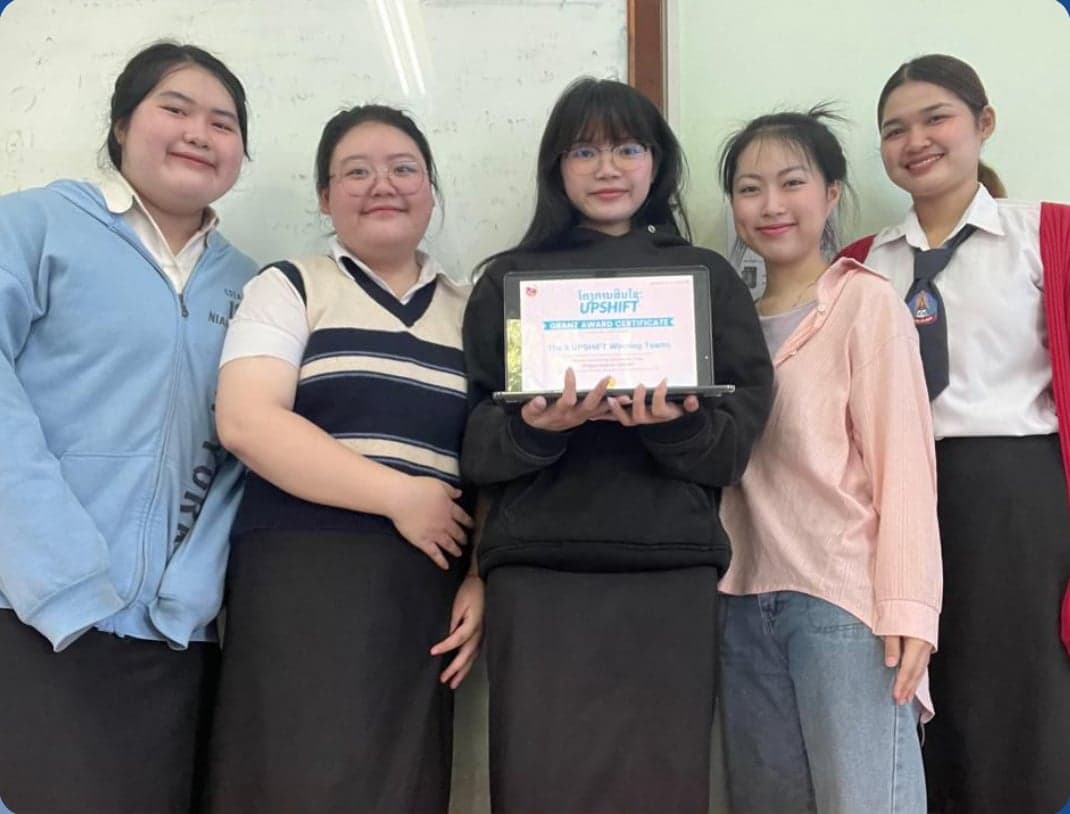 Team Intro, the STOAF soil-testing project from Vientiane — five young women standing indoors in a mix of casual wear and school uniform, one holding a laptop displaying their grant certificate.
