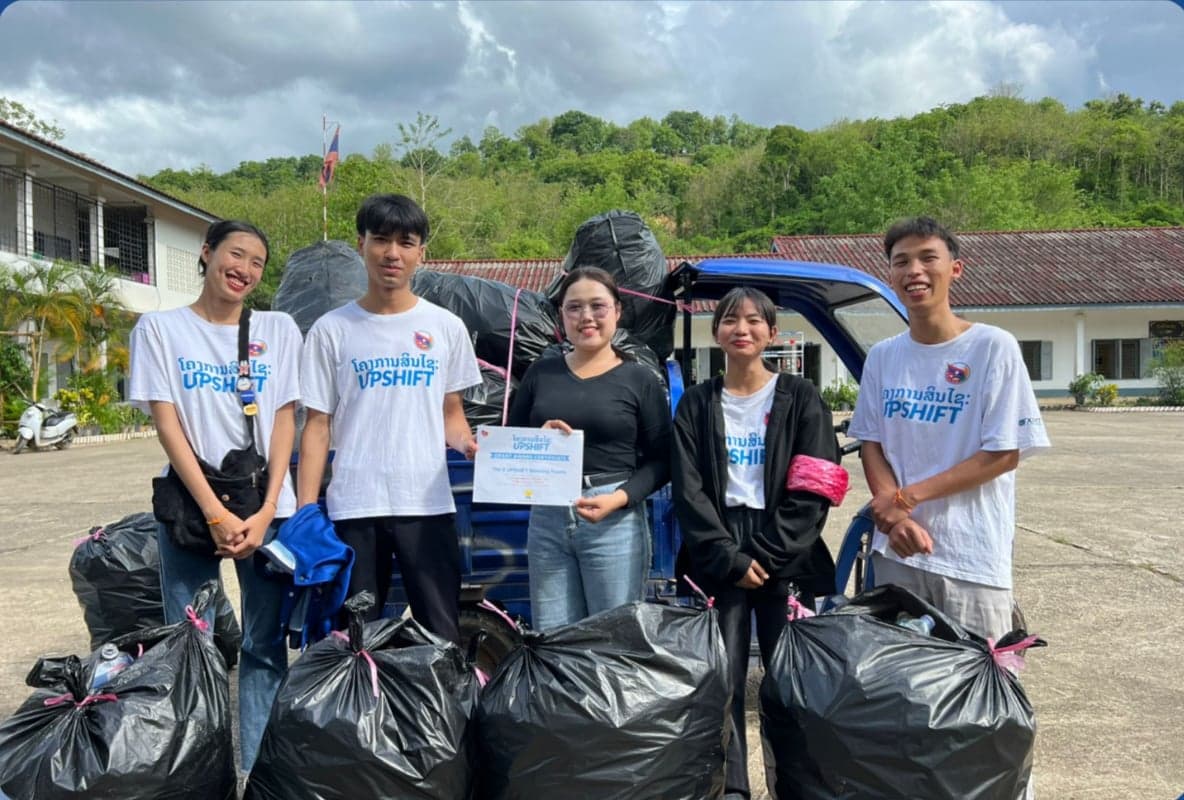 Team Yolo, the Zero Crew project from Luang Prabang — five participants standing outdoors beside a truck loaded with bagged plastic bottles collected through their bottle-exchange programme.